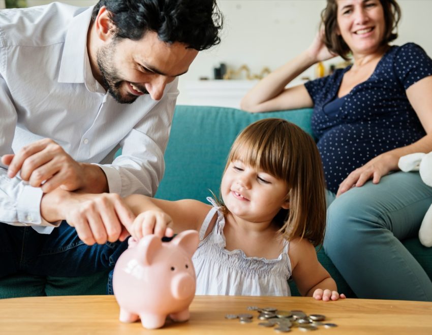 Man and woman with child putting money in to a piggy bank. Links to Help with childcare costs and other support for families