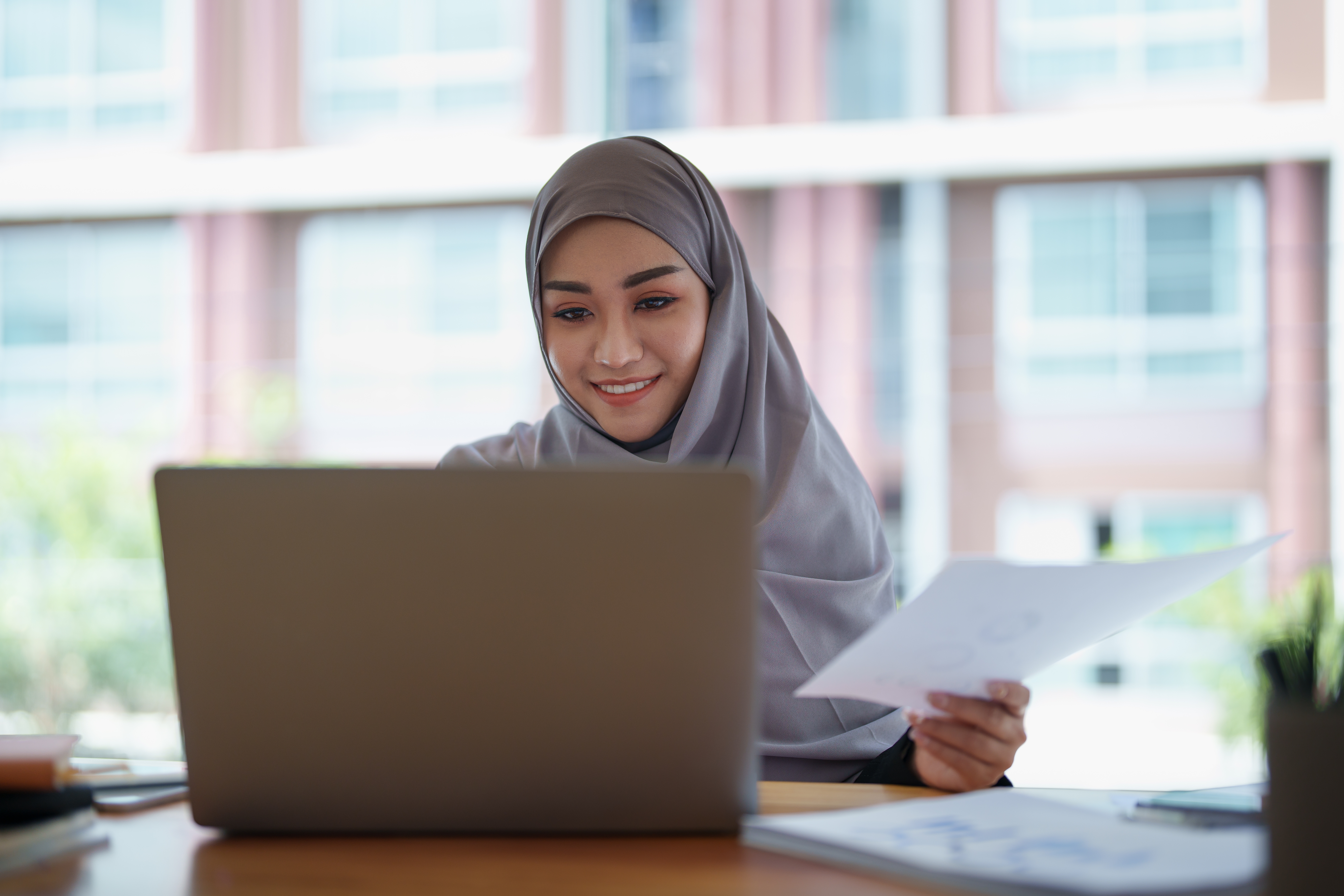 Smiling young Muslim woman working on laptop.