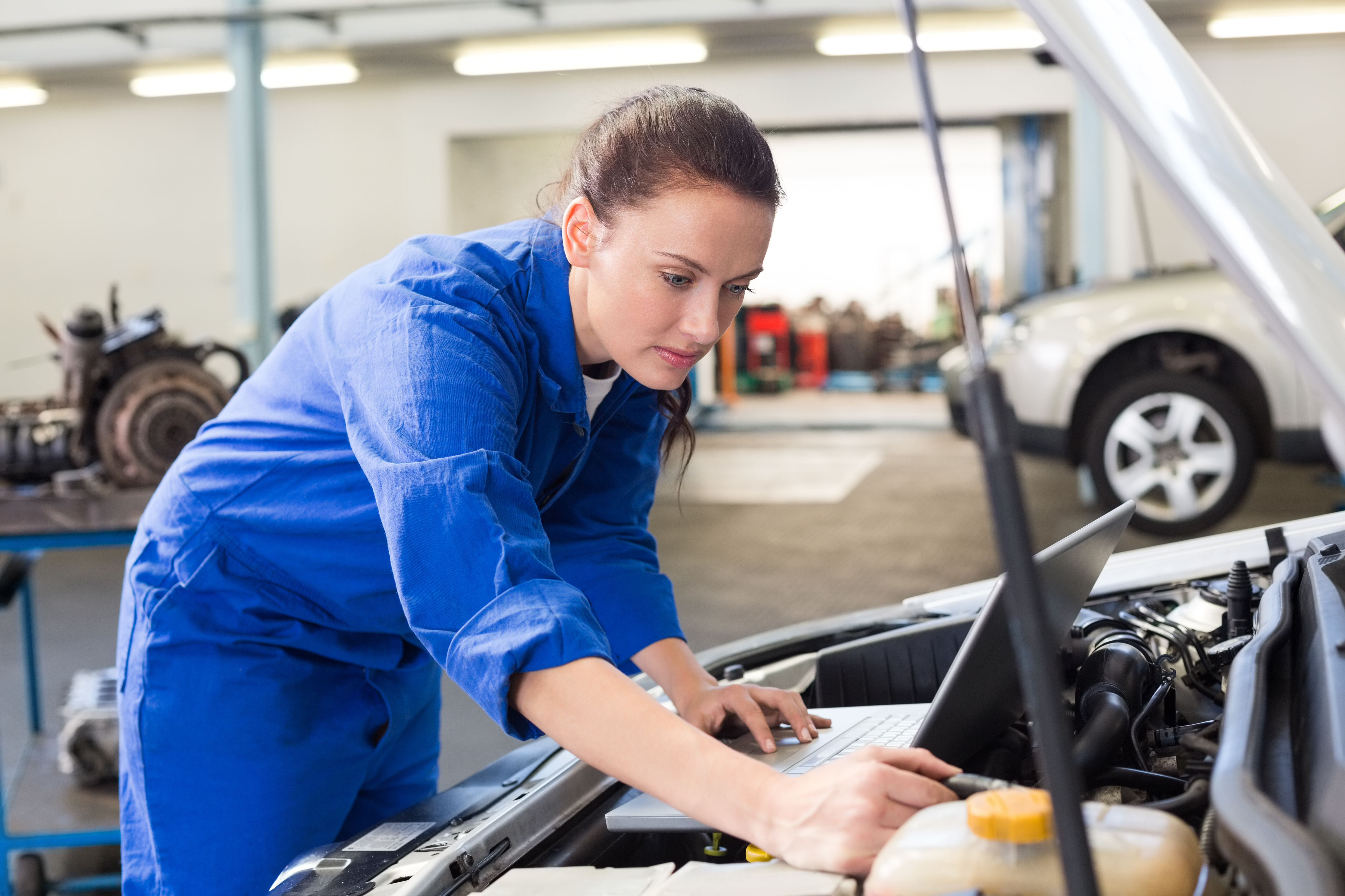 Young woman mechanic with laptop checking engine.